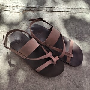 May include: A pair of brown leather sandals with a criss-cross strap design. The sandals have a buckle fastening and a comfortable footbed.