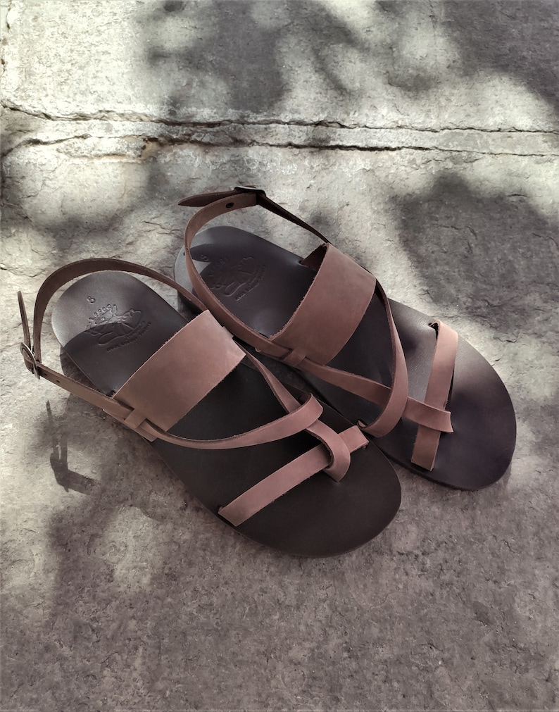 May include: A pair of brown leather sandals with a criss-cross strap design. The sandals have a buckle fastening and a comfortable footbed.