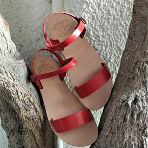 K&ouml;nnte beinhalten: Ein Paar rote Ledersandalen mit Schnallenverschluss. Die Sandalen sind aus weichem Leder gefertigt und bieten einen bequemen Sitz. Die Sandalen werden in Griechenland hergestellt.