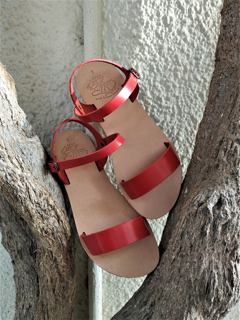 K&ouml;nnte beinhalten: Ein Paar rote Ledersandalen mit Schnallenverschluss. Die Sandalen sind aus weichem Leder gefertigt und bieten einen bequemen Sitz. Die Sandalen werden in Griechenland hergestellt.