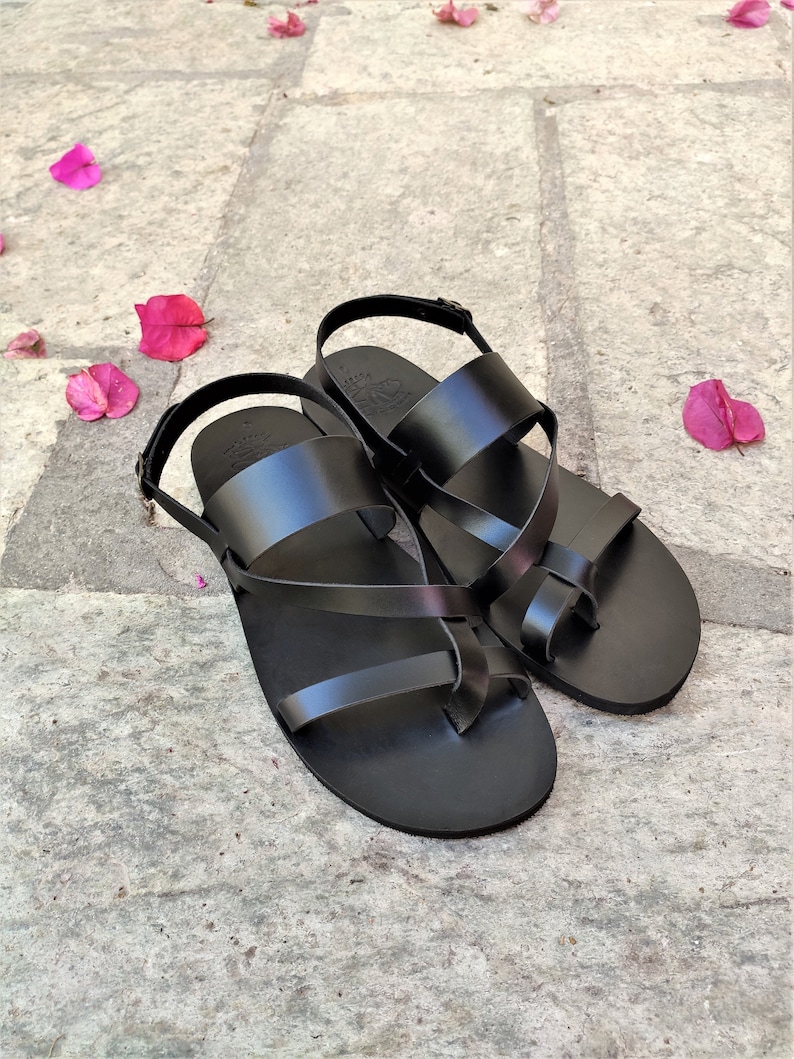 May include: A pair of black leather sandals with criss-cross straps and a buckle fastening.