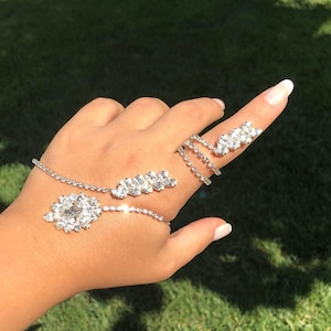 May include: A silver chain bracelet with a large rhinestone cluster charm and a smaller rhinestone cluster ring. The bracelet wraps around the wrist and the ring is worn on the index finger.