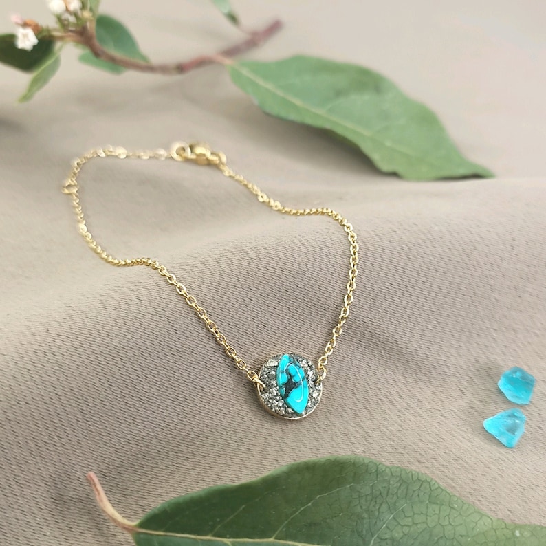 May include: A gold chain bracelet with a turquoise and pyrite stone pendant. The pendant is round and has a bezel setting.