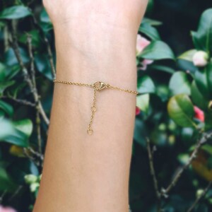 May include: A gold chain bracelet with a lobster clasp closure. The bracelet is shown on a person's wrist.