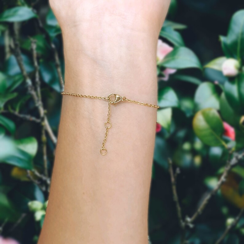 May include: A gold chain bracelet with a lobster clasp closure. The bracelet is shown on a person's wrist.
