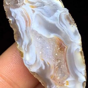 May include: A white agate geode with brown and orange banding. The geode is cut in half and shows the crystal formations inside.