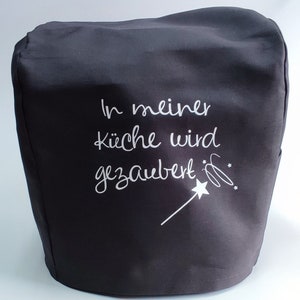 Könnte beinhalten: Eine schwarze Küchengeräteabdeckung mit weißer Schrift, die "In meiner Küche wird gezaubert" und eine Zeichnung eines Zauberstabs zeigt. Die Abdeckung besteht aus einem dunklen Stoff und ist für ein Küchengerät bestimmt.