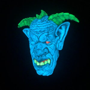 May include: A blue monster mask with glowing green hair and teeth, and red eyes. The mask has a textured surface and large ears. The background is black.