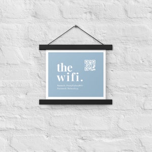 May include: A framed print with the words "the wifi." in a modern font, along with a QR code and network details. The print is light blue and is suspended by a black magnetic frame against a white brick wall.
