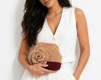 Puede incluir: Bolso de mano de ganchillo en color beige con base burdeos y un gran adorno floral beige a juego. El bolso hecho a mano tiene forma redondeada y cierre de broche.