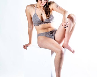 Puede incluir: Conjunto de bikini de ganchillo gris. La parte superior es de estilo halter y la parte inferior es de talle bajo. El conjunto se muestra sobre un fondo blanco. El trabajo de ganchillo es visible.