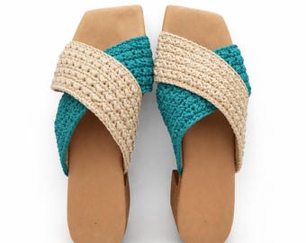 Puede incluir: Un par de sandalias hechas a mano con un diseño de ganchillo beige y turquesa. Las sandalias tienen una suela marrón y un diseño de correas cruzadas. Los zapatos se muestran sobre un fondo blanco.