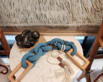 Puede incluir: Objeto decorativo de temática náutica con una gruesa cuerda azul trenzada con asas de madera. La cuerda está conectada con detalles de cuero marrón. También hay una cuerda separada con cuentas de madera y una borla.