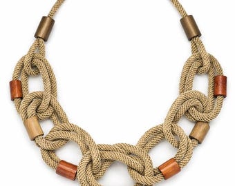 Puede incluir: Un collar dorado con un diseño de cuerda trenzada y secciones anudadas. Incorpora detalles cilíndricos de madera y metal en tonos marrón y verde, creando un accesorio único y texturizado.