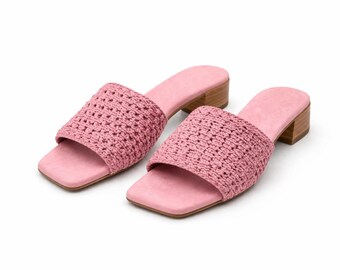 Puede incluir: Un par de sandalias rosas de punta abierta. Las sandalias presentan un diseño de correa tejida y una puntera cuadrada. Tienen una plantilla rosa claro y un pequeño tacón de madera. Los zapatos están sobre un fondo blanco.