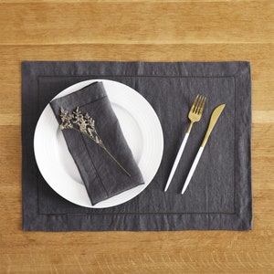 Puede incluir: Un mantel individual de lino gris con un plato blanco, una servilleta gris, un tenedor dorado y un cuchillo dorado. El plato tiene una ramita de flores secas.