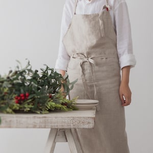 The front looking of flax linen apron which is dressed on behind the desk which has green plants.