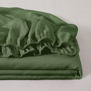 May include: A folded set of olive green bed sheets. The fitted sheet has an elasticized edge. The sheets are made of a soft, textured fabric. The bedding is neatly stacked, with the fitted sheet on top.