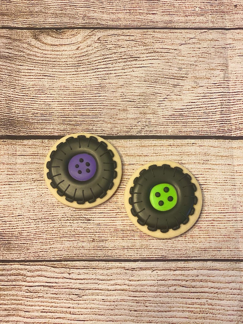May include: Two decorated sugar cookies shaped like tyre rims. One cookie has a purple centre with black dots and the other has a green centre with black dots.