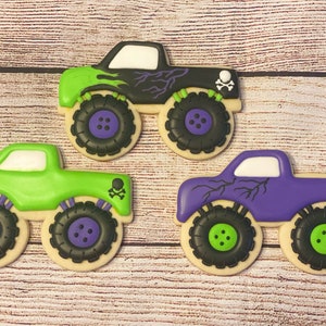 May include: Three monster truck cookies decorated with green, purple and black icing. Each cookie has a skull and crossbones design and a lightning bolt pattern.