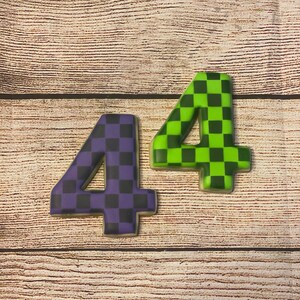 May include: Two cookies shaped like the number four, decorated with a checkered pattern. One cookie is purple and black, the other is green and black.