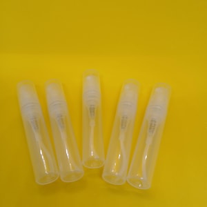 May include: Five clear, empty spray bottles with white spray nozzles are arranged against a bright yellow background. The bottles are cylindrical and appear to be made of plastic. The image is well-lit, highlighting the transparency of the bottles.