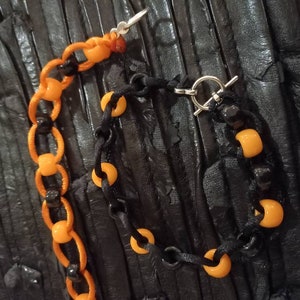 Peut inclure: Un ensemble de collier et de bracelet en perles noires et orange. Le collier a un fermoir argenté et le bracelet a un fermoir à glissière argenté.