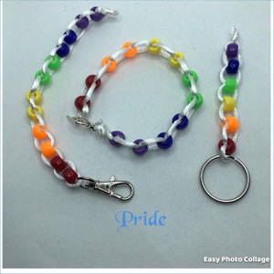 May include: A rainbow beaded keychain with a silver key ring and a rainbow beaded bracelet. The keychain and bracelet are made with white string and colorful beads. The word "Pride" is written in blue below the items.