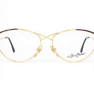 May include: Gold-tone eyeglasses with a cat-eye frame and a signature "Gene Brioni" inscription on the right temple.