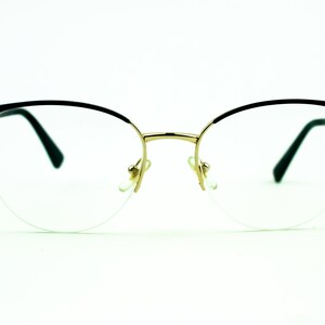 May include: A pair of black and gold spectacles with clear lenses. The glasses have a rounded, cat-eye shape.