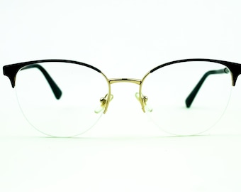 May include: A pair of black and gold spectacles with clear lenses. The glasses have a rounded, cat-eye shape.