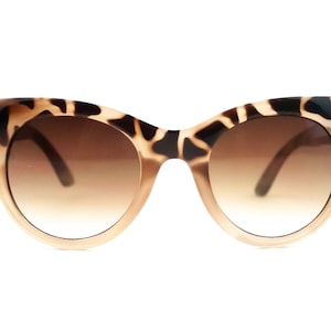 Puede incluir: Un par de gafas de sol de ojo de gato marrones y negras con lentes marrones degradados.