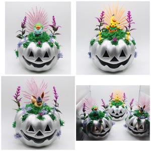 Może przedstawiać: Cztery srebrne dynie w kształcie jack-o'-lantern, ozdobione mchem, kwiatami i figurkami Pokemonów. Dynie mają wyrzeźbioną twarz jack-o'-lantern z trójkątnymi oczami i szerokim uśmiechem.