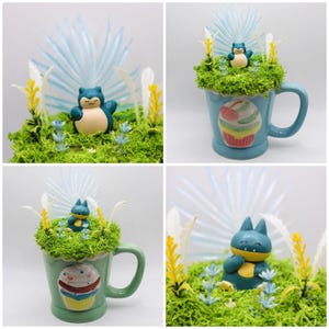 Peut inclure: Quatre images de tasses décorées avec des figurines Pokémon et des plantes artificielles. Les tasses sont bleues et vertes, avec des motifs de cupcakes. Les figurines Pokémon sont Snorlax et Munchlax, dans un paysage de mousse avec des accents bleus et jaunes.