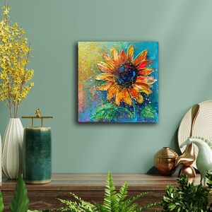 May include: A vibrant painting of a sunflower with orange and yellow petals and a dark blue center. The artwork is on a square canvas, with a textured, impressionistic style. The background is a mix of blue, green, and yellow.