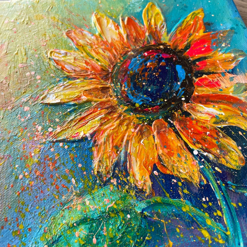 May include: Close-up of a vibrant sunflower painting. The petals are a mix of orange and yellow, with a textured, impasto style. The center is dark blue with colorful accents. The background is a blend of blue and green with paint splatters.