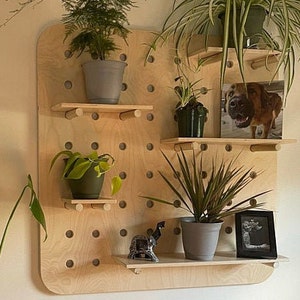 May include: A wooden pegboard with multiple shelves, displaying potted plants, a framed photo of a dog, and a small decorative elephant. The pegboard is made of light-colored wood and has a grid of evenly spaced holes.