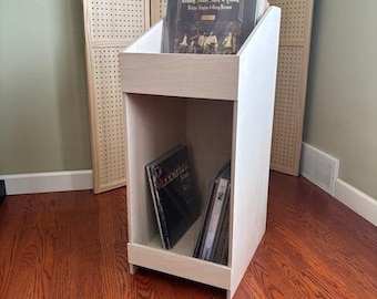 May include: A white wooden record stand with two shelves. The top shelf has a record on it with the title "Grady, Sadie, Jack & Penny" and the bottom shelf has several records stacked on it.