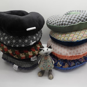 Könnte beinhalten: Ein Stapel von sechs runden Kissen mit verschiedenen Mustern. Die Kissen sind aus Stoff mit einer Vielzahl von Farben und Designs. Eine kleine weiße Katzenfigur steht vor den Kissen.