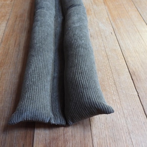 Op de afbeelding: Twee grijze stoffen tochtstoppers, elk met een geribbelde textuur, liggen op een houten vloer.