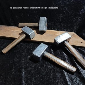 Könnte beinhalten: Vier Hämmer mit rechteckigen, silberfarbenen Metallköpfen und dunkelbraunen Holzgriffen. Die Hämmer sind um ein Stück verwittertes, hellbraunes Holz angeordnet. Der Text "Pro gekauften Artikel erhaltet ihr eine ( 1 ) Requisite" ist sichtbar.