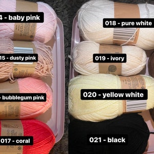 May include: Assortment of yarn skeins in various colors, including baby pink, dusty pink, bubblegum pink, coral, pure white, ivory, yellow white, brown, and black. Each skein is labeled with its color name.