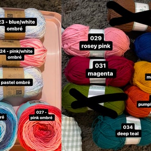 May include: A collection of yarn skeins in various colors, including blue/white ombr&eacute;, pink/white ombr&eacute;, pastel ombr&eacute;, blue ombr&eacute;, pink ombr&eacute;, rosey pink, magenta, royal blue, mustard yellow, pumpkin orange, and deep teal. Each skein is labeled with a color code.