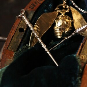 Puede incluir: Un reloj de bolsillo dorado con una cadena y una varita de plata dentro de una caja de madera forrada con terciopelo verde.