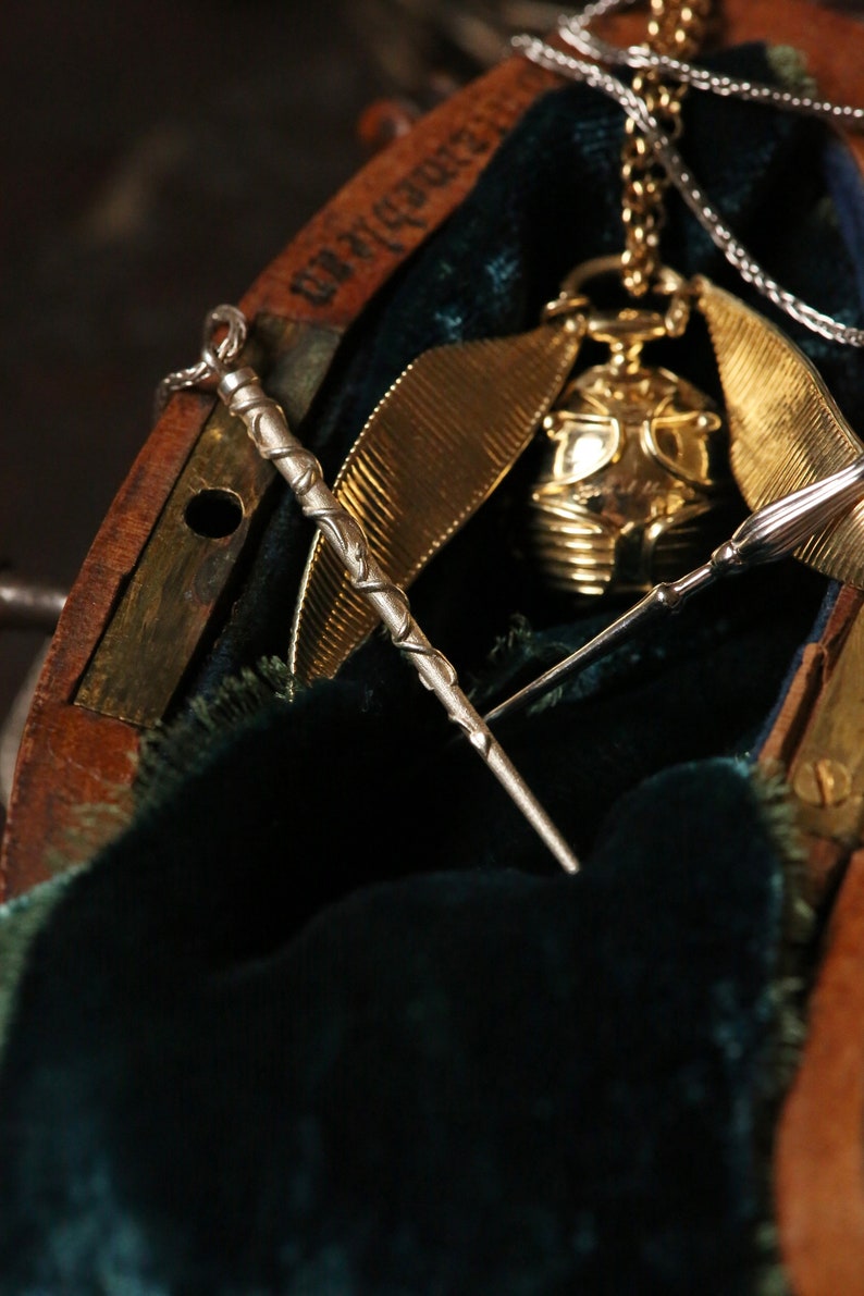 Puede incluir: Un reloj de bolsillo dorado con una cadena y una varita de plata dentro de una caja de madera forrada con terciopelo verde.