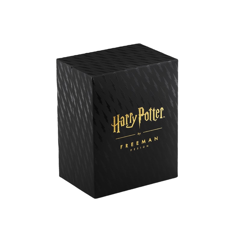 Puede incluir: Caja negra con un logotipo de Harry Potter en relieve dorado y el texto "by FREEMAN DESIGN".