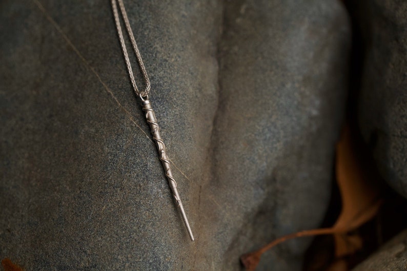 Puede incluir: Un collar de plata con un colgante largo y retorcido en forma de varita.