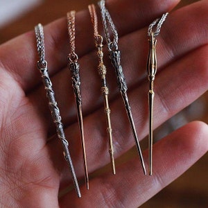 Puede incluir: Cinco collares de plata, oro y oro rosa con diferentes colgantes de varita. Las varitas son detalladas y tienen una variedad de estilos.