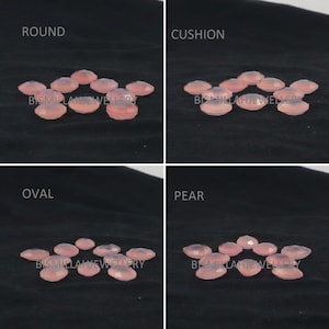 May include: Assortment of pink gemstone cabochons in various shapes, including round, cushion, oval, and pear. The stones are arranged in rows on a black fabric background. The text "Bismillah Jewellery" is visible in the bottom row.