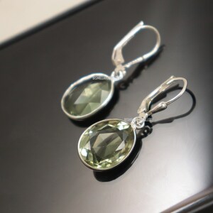 May include: A pair of silver dangle earrings with green oval-shaped gemstones. The earrings have a hook closure.